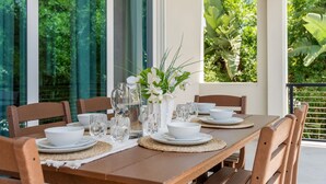 A dining table set with white plates, bowls, glasses, and a pitcher, surrounded by wooden chairs. - Luxury Oceanside Escape – Balcony, Patio & Steps to Indialantic Beach! (Indialantic)