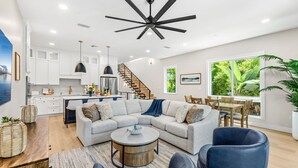 A modern living space with a kitchen, dining area, and a large gray sectional sofa. - Luxury Oceanside Escape – Balcony, Patio & Steps to Indialantic Beach! (Indialantic)
