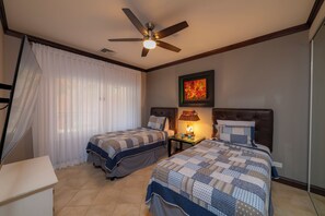A hotel room with two beds, a ceiling fan, a nightstand with a lamp, and a painting on the wall. - AltaVista 4C 3 bdr Ocean View in Los Suenos (Playa Herradura)