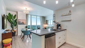 Une cuisine moderne équipée d’un lave-vaisselle, un coin repas avec une table et des chaises, une grande fenêtre offrant une vue agréable et un lustre.