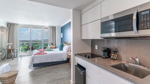 A modern hotel room with a large bed, a kitchenette with a microwave, and a view of the city.