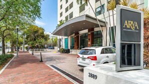 A hotel entrance with a modern design, a car parked in front, and a sign indicating the hotel's name.