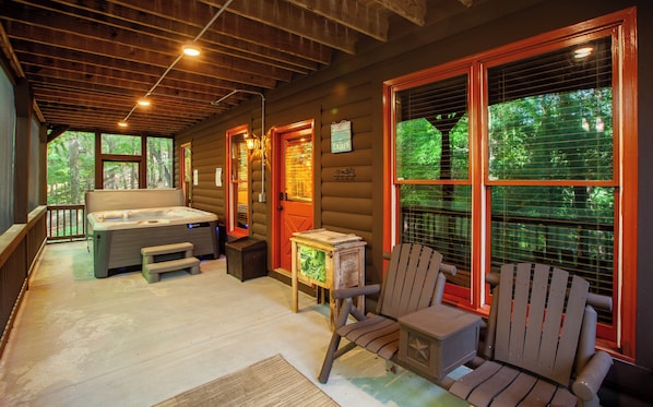 A cabin with a hot tub, a deck chair, and a wooden table.