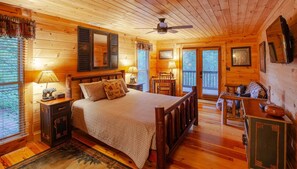 A wooden cabin bedroom with a bed, bedside lamps, a desk, and a chair. - Firefly Hollow | Hot Tub, Game Room & Fire Pit | Pet-Friendly | Sleeps 10 (Blue Ridge)