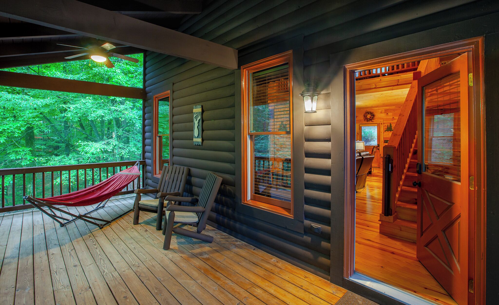 A wooden cabin with a deck, a hammock, and two chairs.