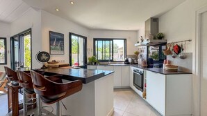 A modern kitchen with a central island, bar stools, a large window, and a view of greenery outside.