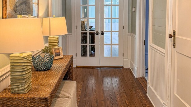 A hallway with a wooden floor, a wicker bench, a lamp, and a framed picture on a console table. - Historic Coastal Retreat: 3‑BR Cape Cod Cottage w/ Courtyard, Porch & Bay Access (Apalachicola)