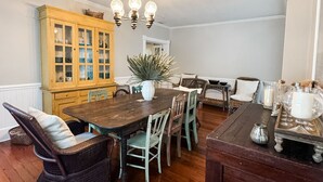 A dining area with a wooden table, wicker chairs, a cabinet, and a chandelier. - Historic Coastal Retreat: 3‑BR Cape Cod Cottage w/ Courtyard, Porch & Bay Access (Apalachicola)