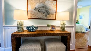 A room with a wooden desk, two upholstered stools, a framed map artwork, and two lamps. - Historic Coastal Retreat: 3‑BR Cape Cod Cottage w/ Courtyard, Porch & Bay Access (Apalachicola)