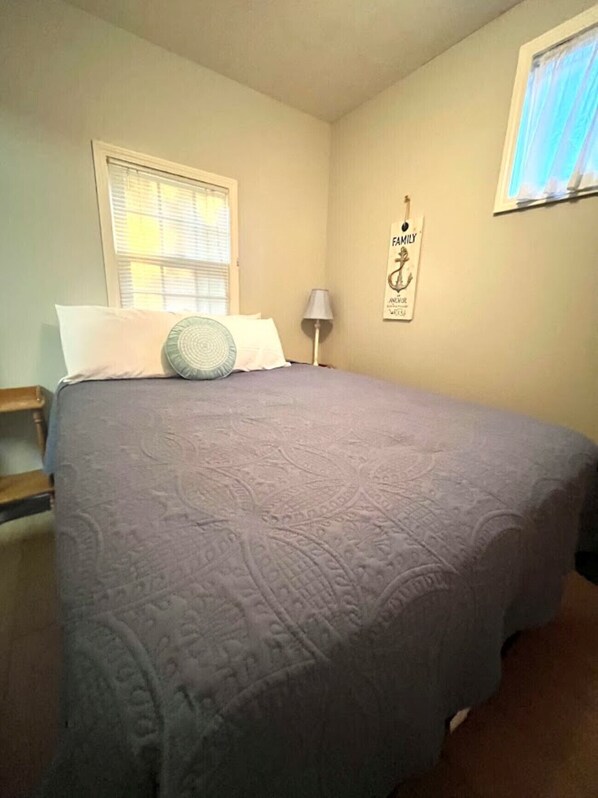 A bedroom with a bed, a window with blinds, a wall-mounted lamp, and a framed poster.