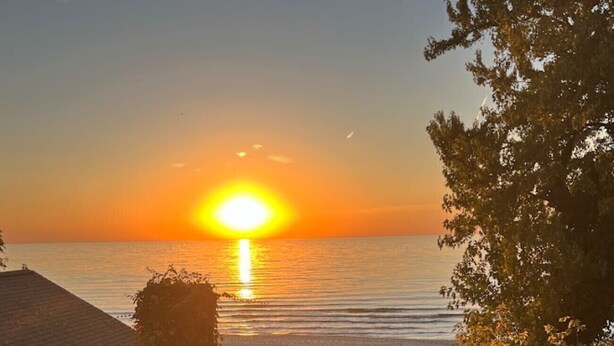 Eine Holztreppe führt zu einem Strand, im Hintergrund ist ein Sonnenuntergang zu sehen.