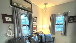 Ein Wohnzimmer mit einer schwarzen Ledersofa, einem kleinen weißen Beistelltisch, einer Lampe und einer Deckenleuchte.