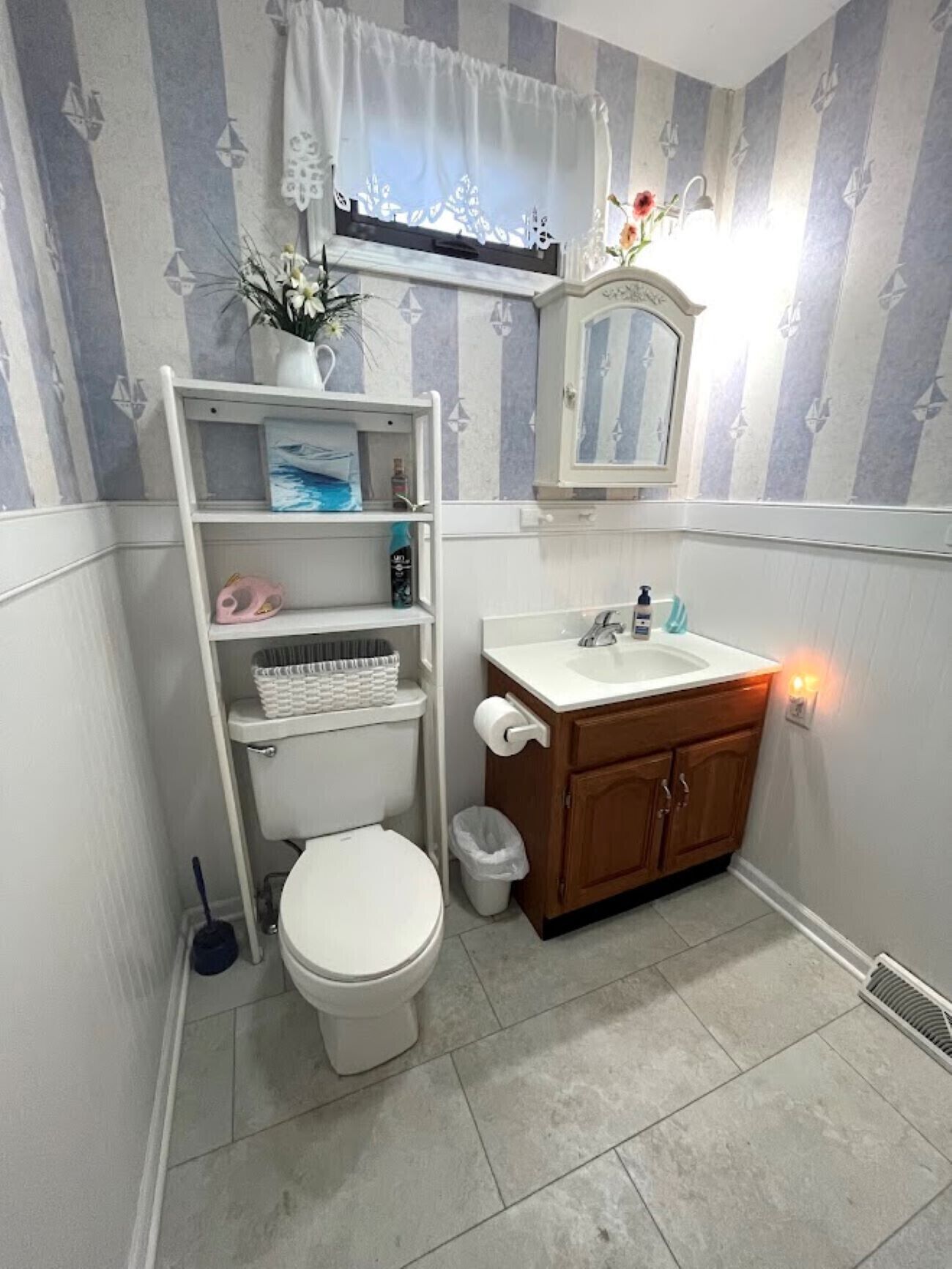 Une salle de bain comprenant des toilettes, une étagère avec des articles de toilette, un miroir et un lavabo.