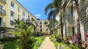 Un camino bordeado de palmeras y vegetación, que lleva a un edificio con varios balcones y ventanas.