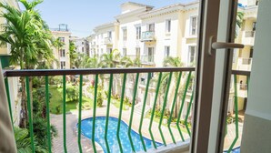 Un balcón con vistas a una piscina, rodeado de vegetación y edificios de varios pisos.