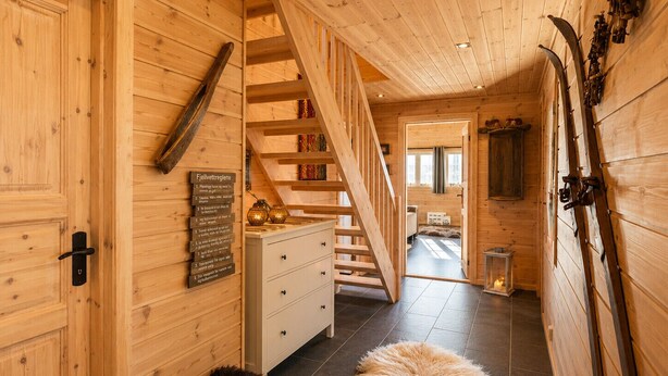 Un interior de madera con una escalera, un cartel con texto, un felpudo de piel y un perro.