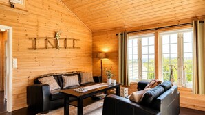 Interior acogedor de una cabaña con techo de madera, un sofá, una mesa de centro y vistas amplias a través de grandes ventanales.