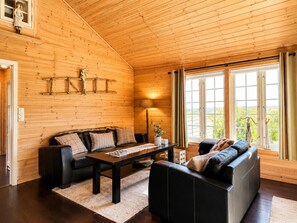 Interior acogedor de una cabaña con techo de madera, un sofá, una mesa de centro y vistas amplias a través de grandes ventanales.