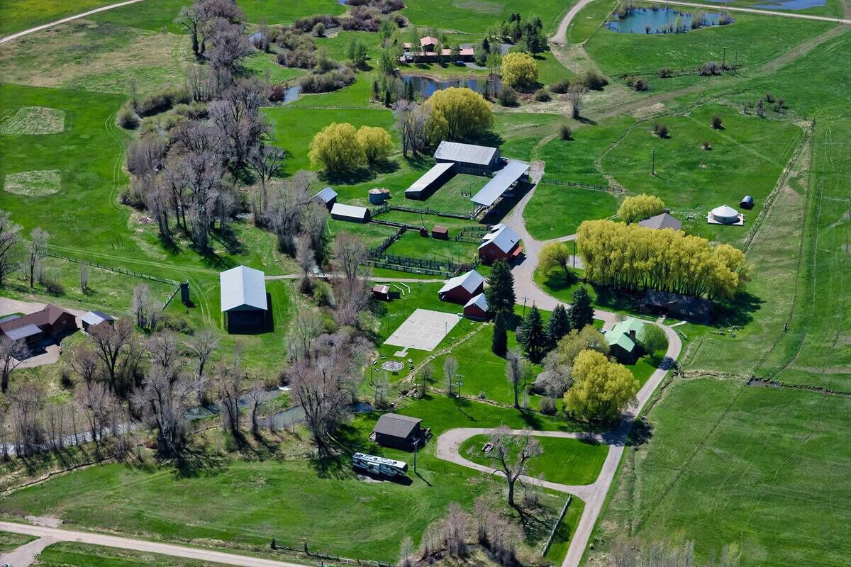 Vista aérea de una propiedad rural con varias construcciones, incluyendo establos y casas, rodeada de campos verdes y árboles.