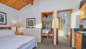 Un dormitorio con cama, mesita de noche, lámpara y un cuadro en la pared. Hay una puerta que da a un baño con inodoro y lavabo.