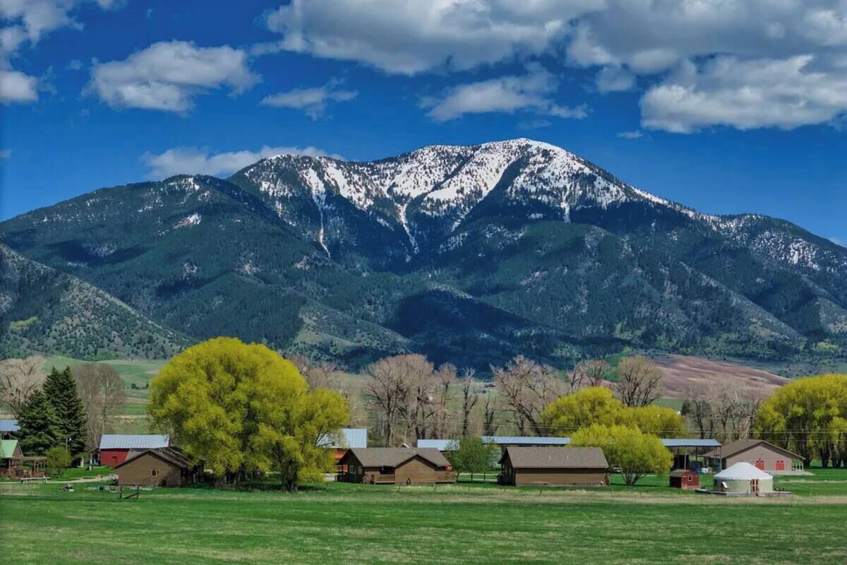 A mountain with snow-capped peaks, a green field, and several buildings with red roofs.
