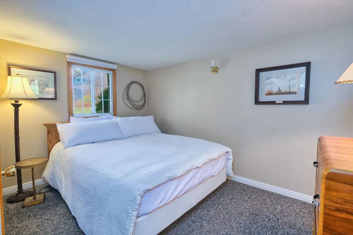 Un dormitorio con cama, lámpara, ventana y un cuadro en la pared.