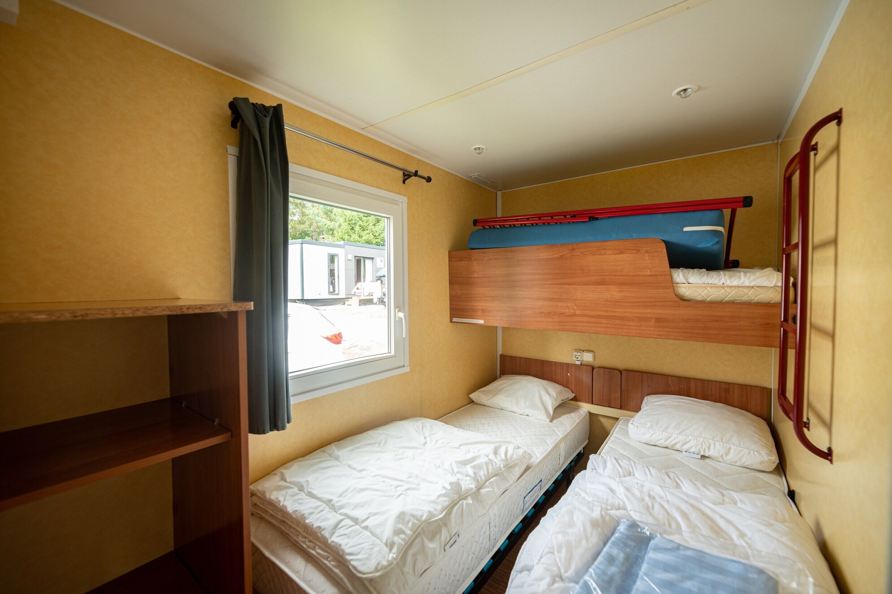 Quarto pequeno com beliches e uma janela.