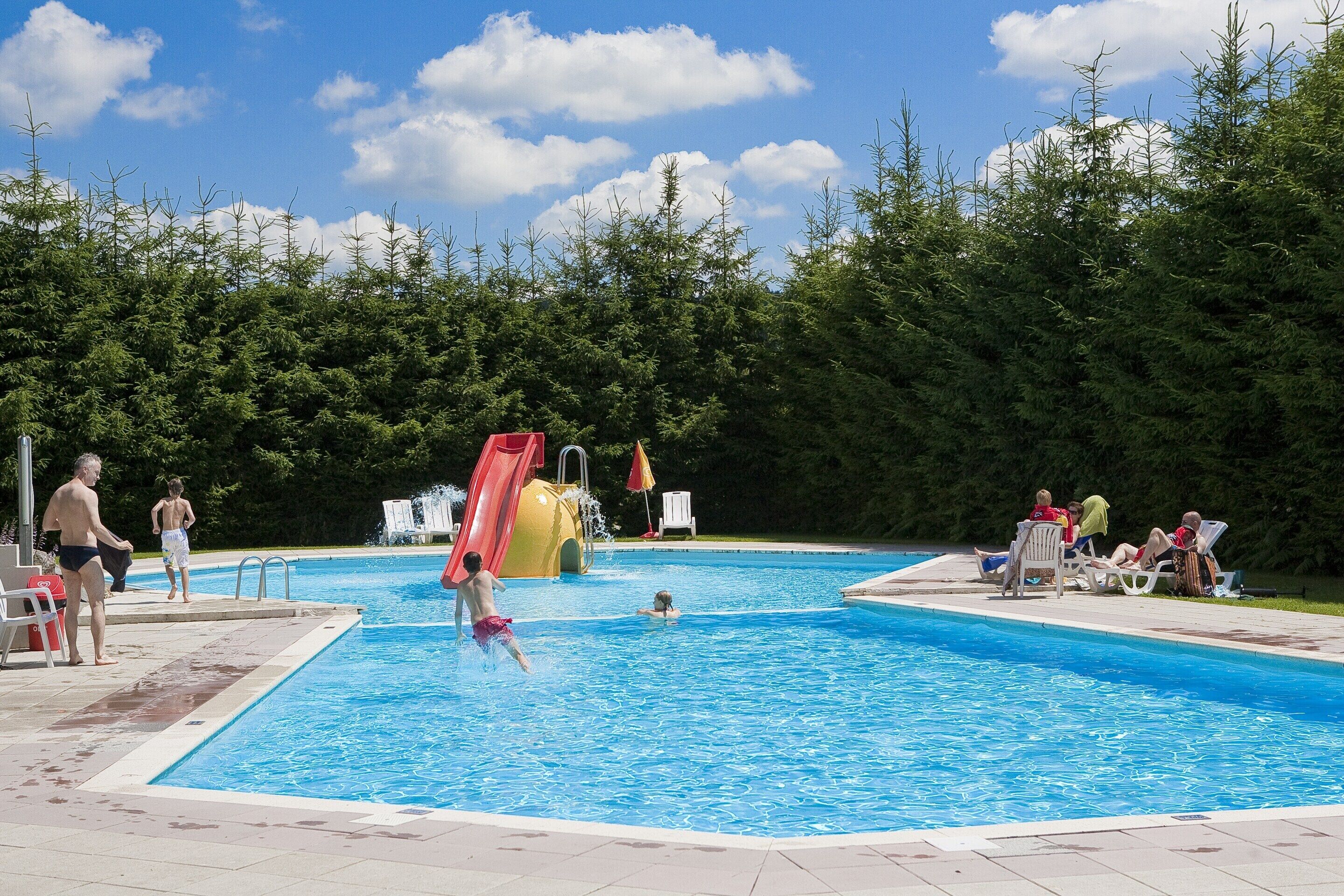 Una piscina con tobogán y sillas de descanso.