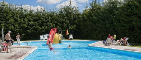 Una piscina con tobogán y sillas de descanso.