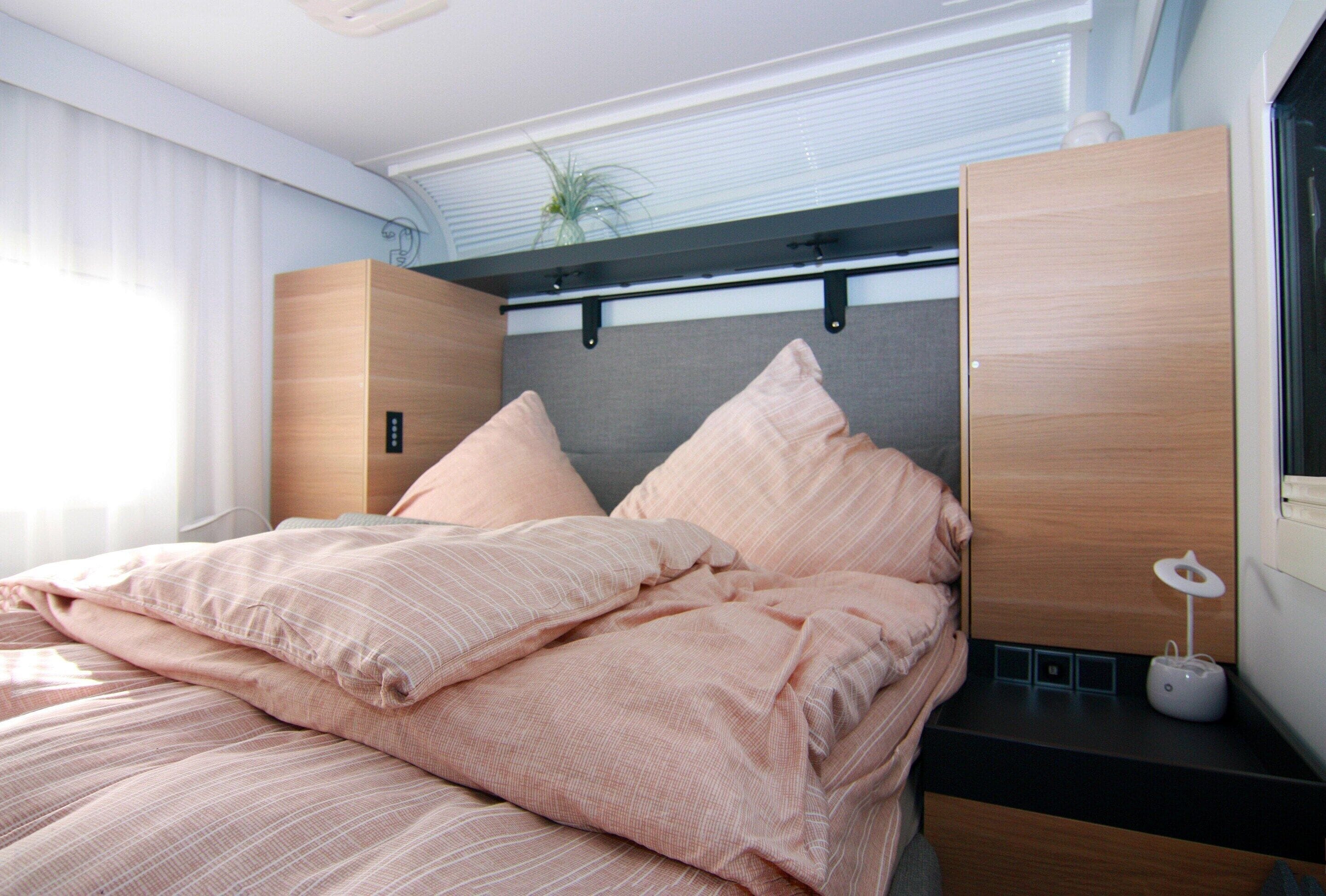 A modern bedroom with a bed, wooden headboard, and a bedside table with a lamp.