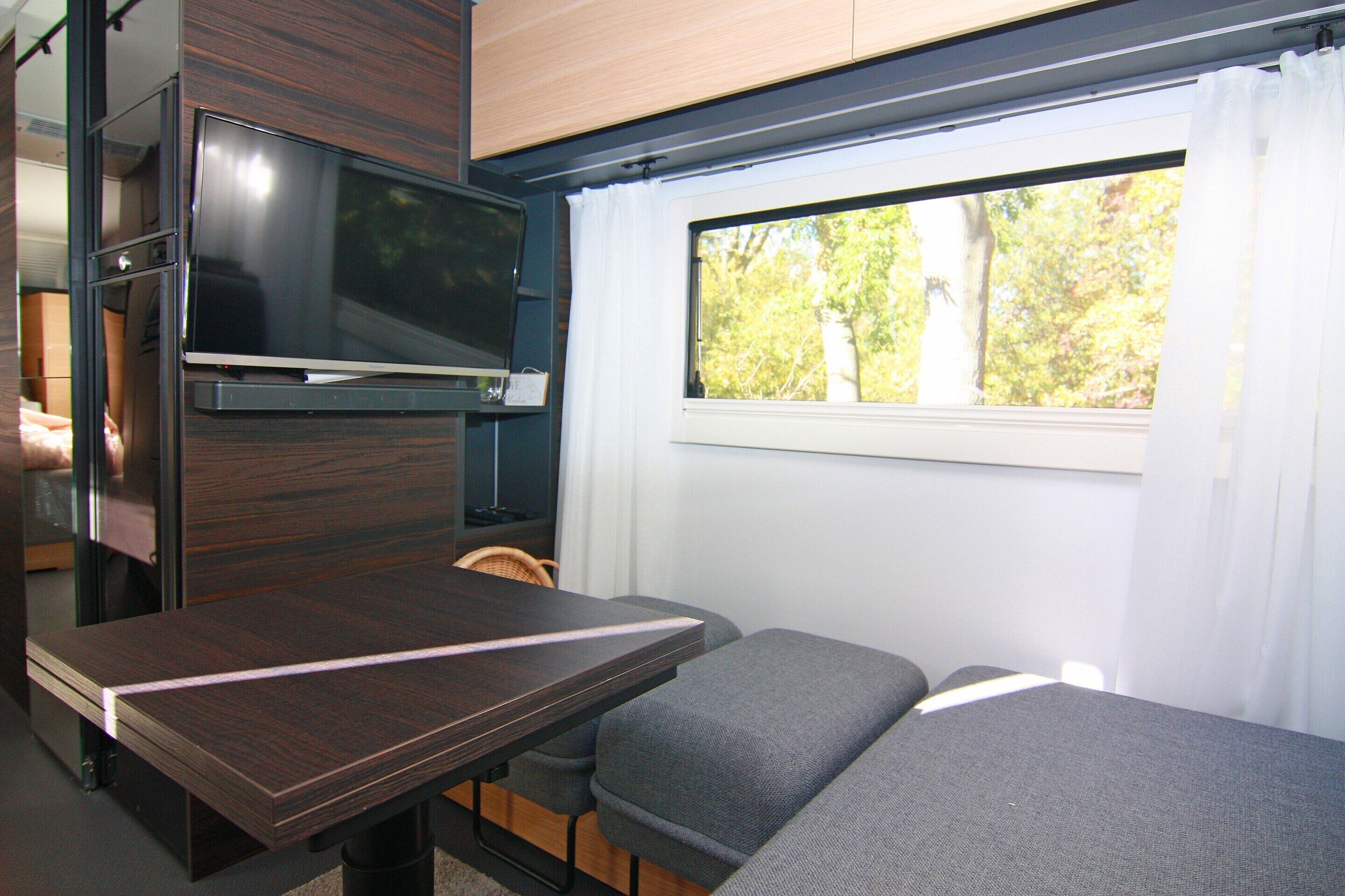 A compact RV interior with a flat-screen TV, a small table, and a sofa.