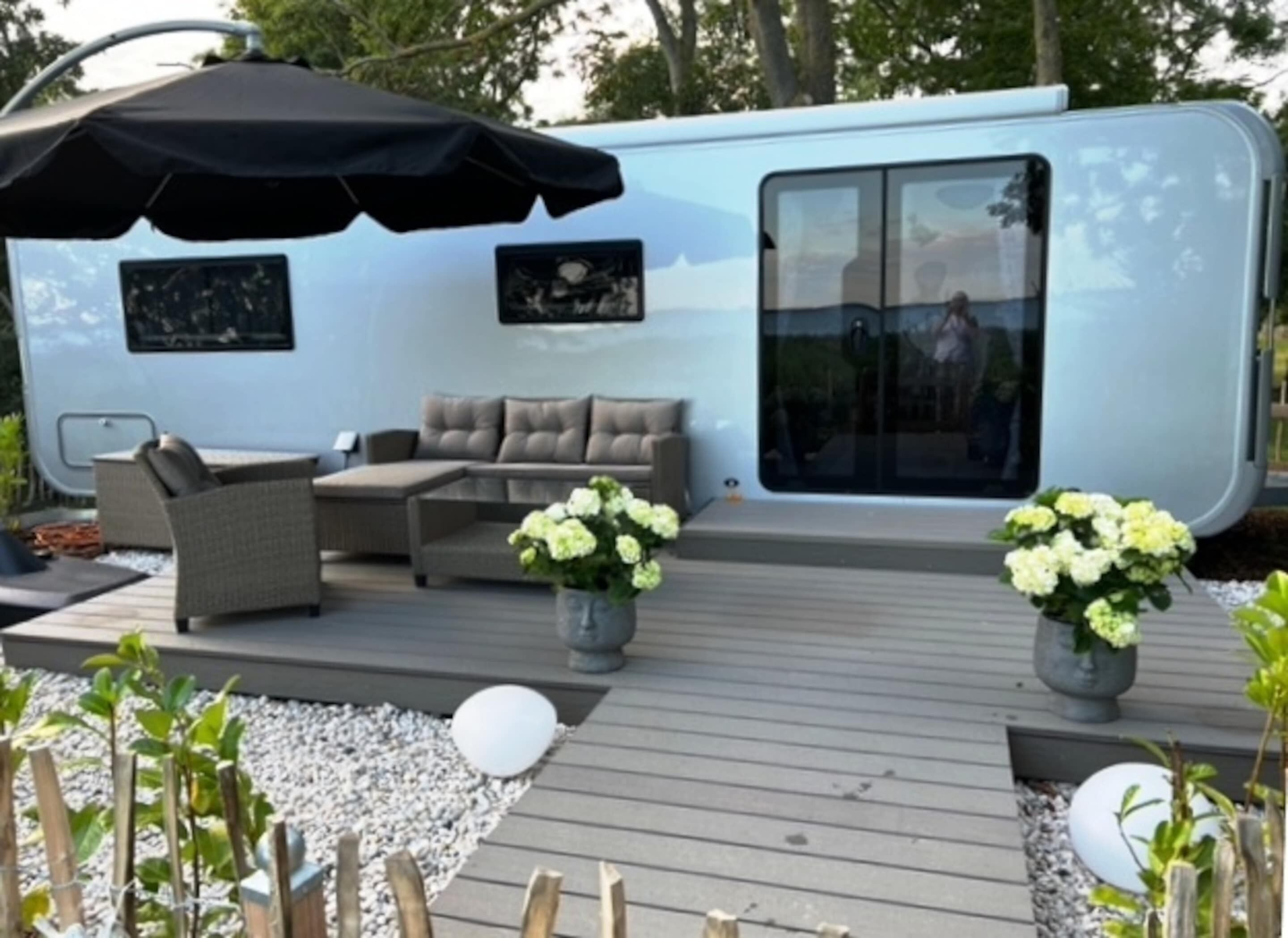A modern RV with a deck area featuring outdoor furniture and potted plants.