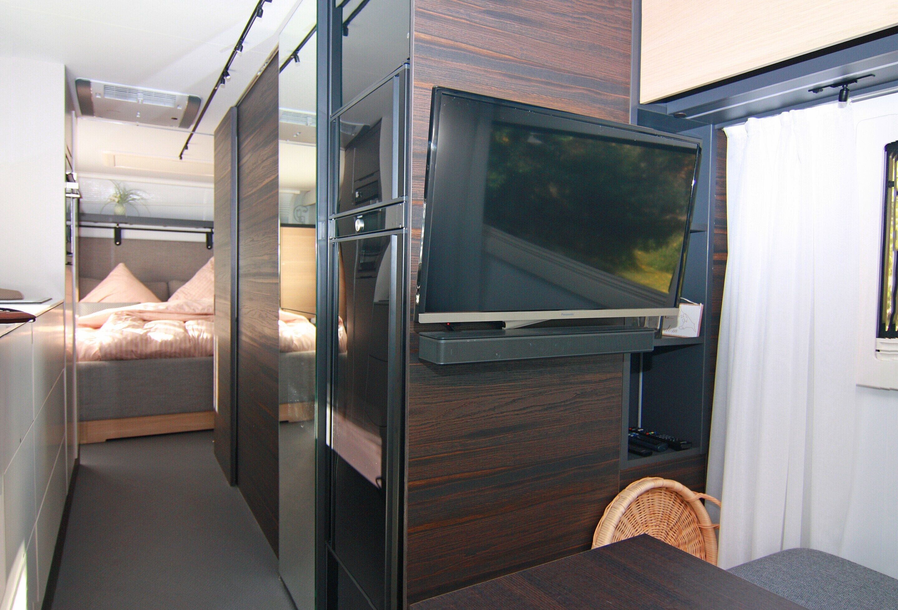 A compact living space with a bed, a built-in TV, and a small dining area.