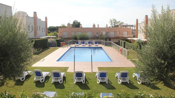 Una piscina con sillas de descanso, rodeada de vegetación y edificios.