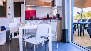 Een moderne keuken met witte en rode kastjes, een ingebouwde magnetron, en een eethoek met witte stoelen en een tafel gedekt voor twee personen.