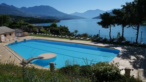 A rectangular swimming pool with a small deck area, surrounded by lounge chairs and a fence. - Apartment on Lake Serre-poncon With Pool (Chorges)