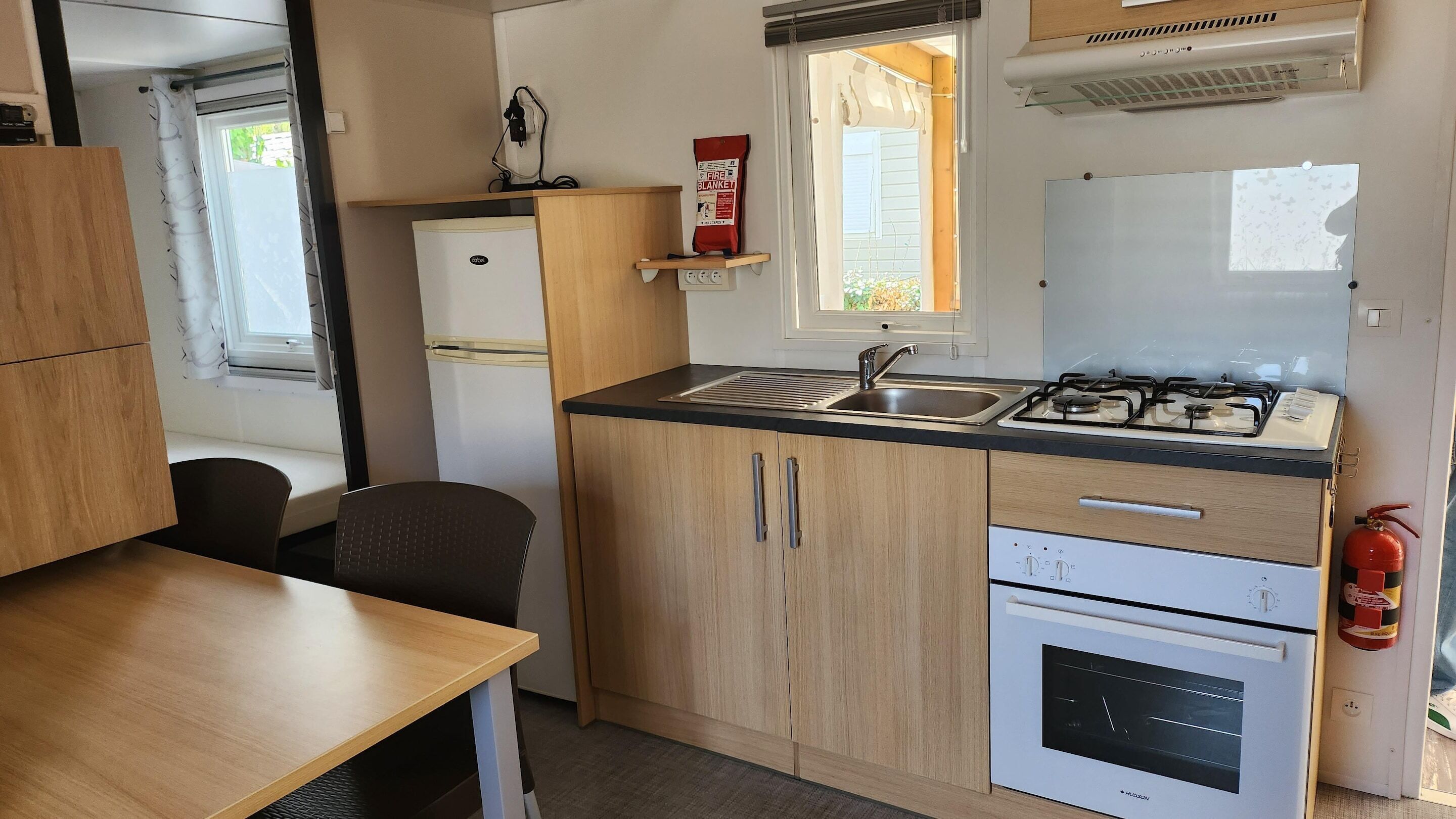 A compact kitchen with a sink, stove, and oven, wooden cabinets, and a window with a view.