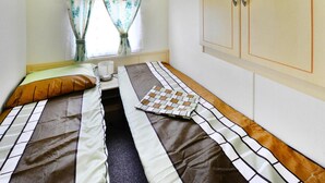 A single bed with a striped bedspread, a pillow, and a bedside table with a lamp. - Mobile Home by the Lake Beach (Malechowo)