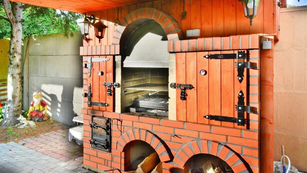 A brick outdoor oven with a chimney, a wooden roof, and a small table nearby. - Mobile Home by the Lake Beach (Malechowo)