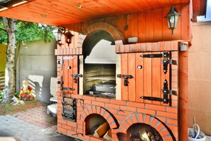 A brick outdoor oven with a chimney, a wooden roof, and a small table nearby. - Mobile Home by the Lake Beach (Malechowo)