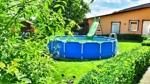 A backyard with a blue above-ground pool, a green slide, and a house in the background. - Mobile Home by the Lake Beach (Malechowo)
