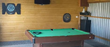 Una mesa de billar con dos dardos y un televisor colocado en la pared.