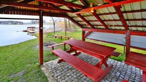A covered picnic area with a table and benches, overlooking a body of water. - Mobile Home by the Lake Beach (Malechowo)