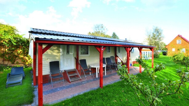 A covered outdoor seating area with chairs and a table, adjacent to a house with a red roof. - Mobile Home by the Lake Beach (Malechowo)