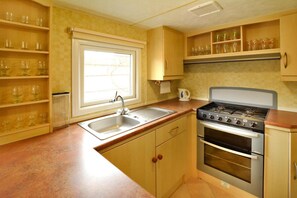 Een kleine keuken met een spoelbak, fornuis en planken voor glaswerk.