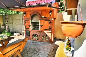 An outdoor kitchen area with a brick oven, wooden cabinets, and a hanging pot rack. - Mobile Home by the Lake Beach (Malechowo)