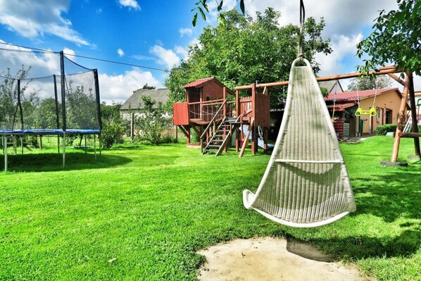 A backyard with a trampoline, a swing, and a wooden playhouse. - Mobile Home by the Lake Beach (Malechowo)