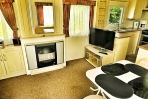 A compact kitchen with a stove, sink, and a flat-screen TV. - Mobile Home by the Lake Beach (Malechowo)
