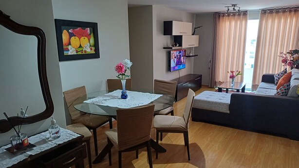 A modern living room with a glass dining table, comfortable seating, a flat-screen TV mounted on the wall, and a sofa with cushions. - Comfortable family apartment in the center of Magdalena del Mar. (Magdalena del Mar)