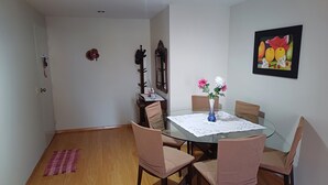 A dining area with a glass table, four chairs, a vase with flowers, a framed picture on the wall, and a wooden floor. - Comfortable family apartment in the center of Magdalena del Mar. (Magdalena del Mar)